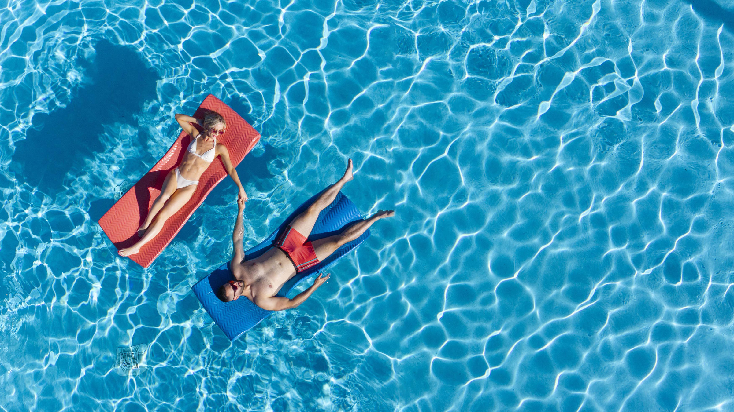 Overhead aerial of a couple floating on a sparkling blue pool